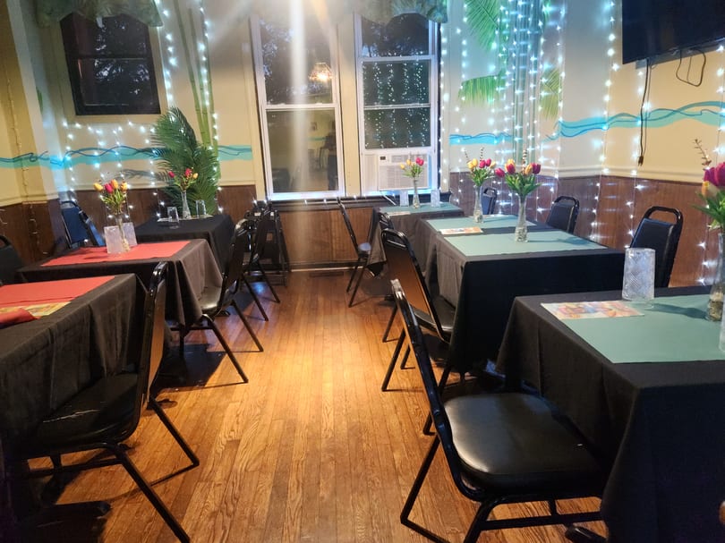 Restaurant dining room with black-draped tables, colorful tulips, string lights, and painted tropical decor.