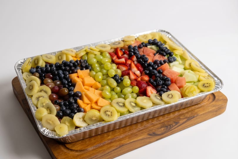 A large catering tray filled with colorful fresh fruit, including kiwi, grapes, blueberries, strawberries, and melon.