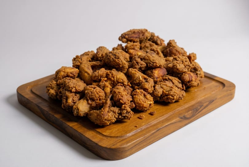 A large pile of crispy, golden-brown fried chicken pieces on a wooden serving board.