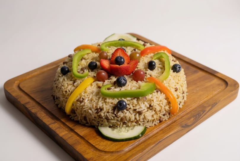Rice and lentils dish topped with colorful bell peppers, blueberries, grapes, strawberries, and cucumber.